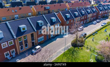 Contemporary townhouses neatly lined along a serene street in a Dutch suburban neighborhood. Featuring solar panels for sustainable energy, this vibrant area promotes comfortable family living. Stock Photo