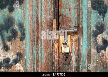 A detail of a bolted double door with new padlock on old rusted fittings. The doors have layers of exposed paintwork and stains Stock Photo