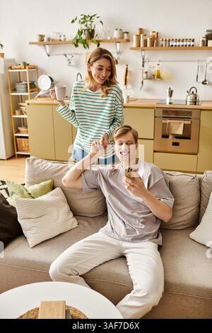 A couple enjoys playful moments at home, smiling over coffee and chatting happily. Stock Photo