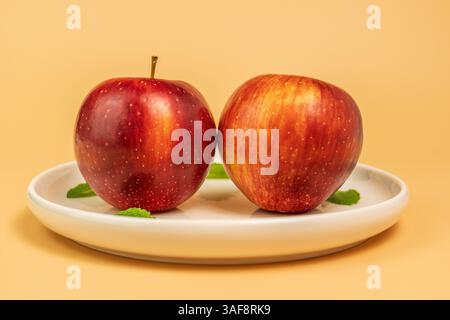 Two Red Apples with Mint Leaves on White Plate with creamy background - Side View Stock Photo