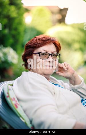 Candid portrait of happy senior woman. Relaxed retired woman with glasses, enjoying serene day in her backyard during retirement Stock Photo