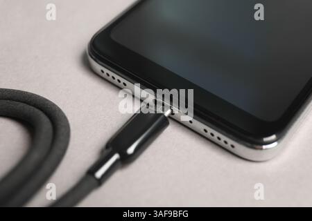 USB charge cable connected to smartphone on light grey background, closeup Stock Photo