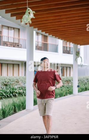 Asian man walks thoughtfully in hotel modern corridor, looking onward toward his vacation Stock Photo
