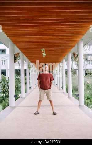 Man standing in modern architecture walkway with symmetrical lines and tropical plants. Tourist on vacation Stock Photo