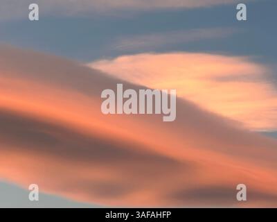 Captivating view of layered clouds painted in vibrant pink and orange hues against a blue sky. Stock Photo