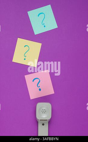 Retro handset and question marks on memo pieces of paper. Call center. Hotline. Purple studio background, top view. Stock Photo