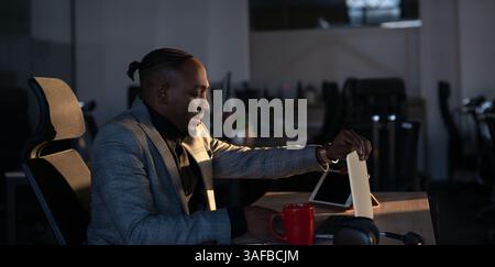 Young African-American IT manager, programmer or web developer closing his laptop in a dimly lit office. Concept of late work, business decision Stock Photo
