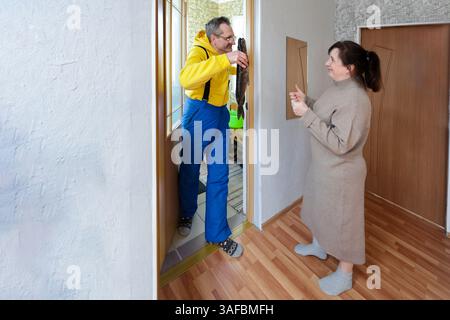 Man is holding large fish, perhaps pike, woman is standing by doorway, both are indoors, on parquet floor, in brightly lit hallway. Stock Photo
