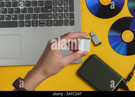 Female hand holds SD memory card on a background of gadgets. Top view Stock Photo