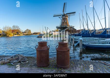 Typical dutch scenery with two vintage rusty milk cans and the historical windmill in the village of Woudsend in Province of Friesland Stock Photo