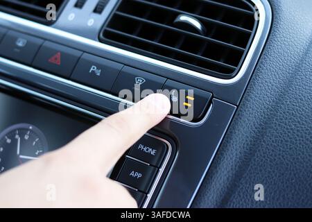 Close-up of finger pressing heated seat button in modern car interior control panel. Stock Photo