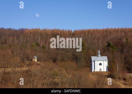 A small white church is surrounded by trees and a large moon is visible in the sky. The scene is peaceful and serene, with the moon casting a soft glo Stock Photo