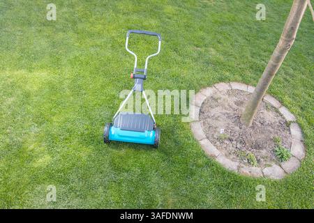 A vibrant garden scene featuring a blue manual lawn mower on a freshly mowed, lush green lawn, symbolizing gardening care, outdoor maintenance, and pr Stock Photo