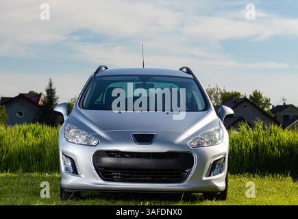 A modern silver car is parked in a field under a clear blue sky, showcasing its stylish design and headlight symmetry. Stock Photo