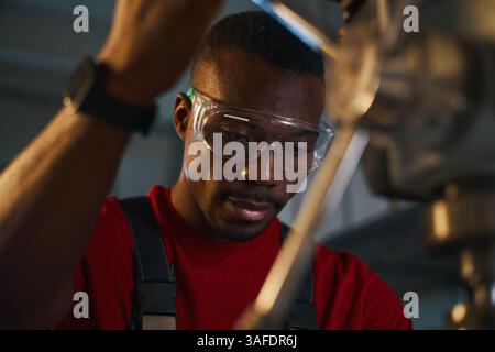 African American manual worker in protective eyeglasses working on lathe Stock Photo