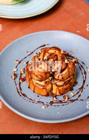 Cinnamon bun with caramel sauce and nuts served on a blue ceramic plate Stock Photo