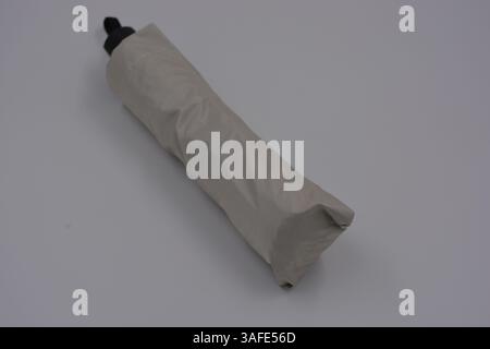 Beautiful new beige, gold, white, light umbrella with black handle, light cover, black lining from water and rain is located on a white plastic. Stock Photo