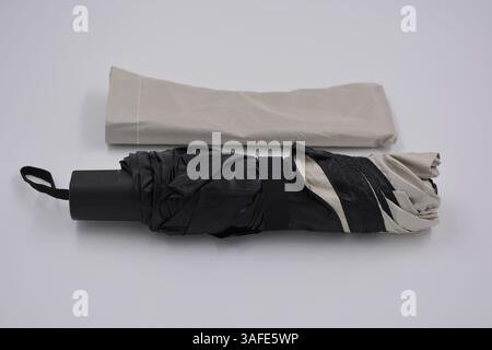 Beautiful new beige, gold, white, light umbrella with black handle, light cover, black lining from water and rain is located on a white plastic. Stock Photo