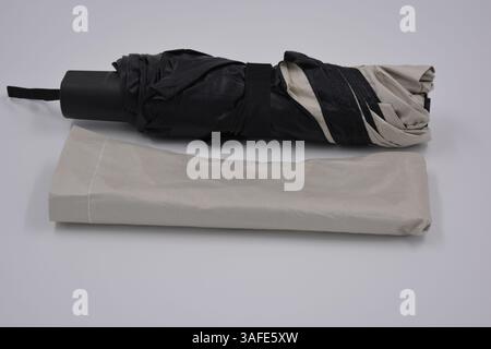 Beautiful new beige, gold, white, light umbrella with black handle, light cover, black lining from water and rain is located on a white plastic. Stock Photo
