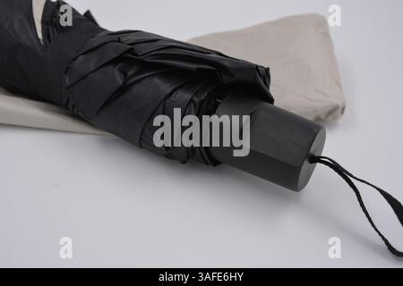 Beautiful new beige, gold, white, light umbrella with black handle, light cover, black lining from water and rain is located on a white plastic. Stock Photo