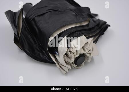 Beautiful new beige, gold, white, light umbrella with black handle, light cover, black lining from water and rain is located on a white plastic. Stock Photo