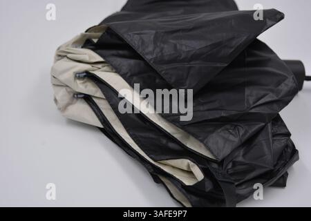 Beautiful new beige, gold, white, light umbrella with black handle, light cover, black lining from water and rain is located on a white plastic. Stock Photo