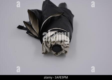 Beautiful new beige, gold, white, light umbrella with black handle, light cover, black lining from water and rain is located on a white plastic. Stock Photo