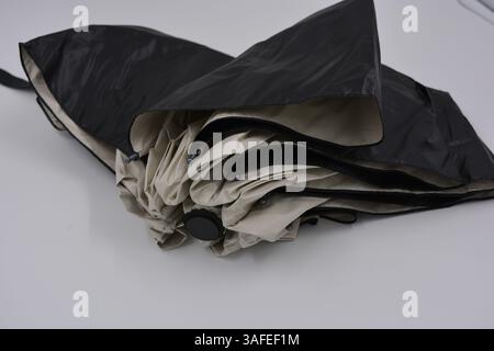 Beautiful new beige, gold, white, light umbrella with black handle, light cover, black lining from water and rain is located on a white plastic. Stock Photo