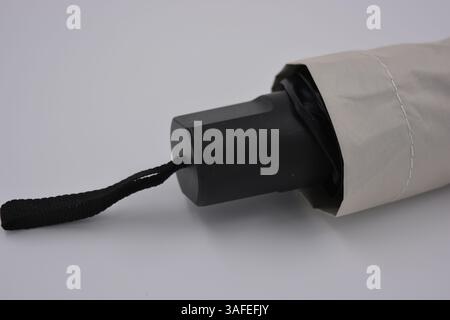 Beautiful new beige, gold, white, light umbrella with black handle, light cover, black lining from water and rain is located on a white plastic. Stock Photo