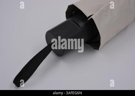 Beautiful new beige, gold, white, light umbrella with black handle, light cover, black lining from water and rain is located on a white plastic. Stock Photo