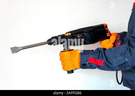 workman with a rotary hammer. Hands in protective gloves with hammer drill perforator. Copy space. Stock Photo