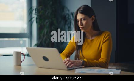Focused young analyst or marketing manager typing on a laptop in a modern office with natural light. Concept of professional work, digital Stock Photo