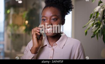 African American businesswoman smiling talking cellphone in office ethnic girl business woman positive student consultant call mobile phone indoors Stock Photo