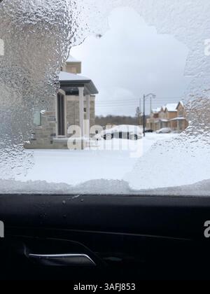 A layer of ice on car window after winter ice storm overlooking snowy residential neighbourhood Stock Photo