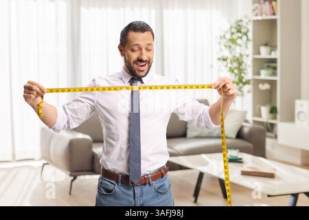 Man with a yellow measure tape standing in a living room and smiling Stock Photo