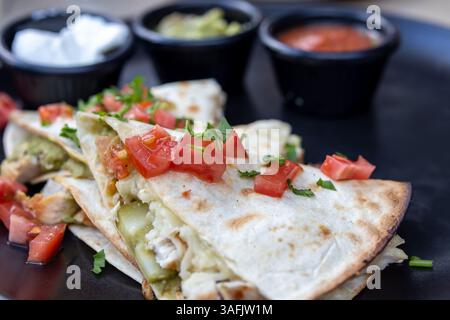 Delicious Chicken Quesadilla with Toppings on a Black Plate Stock Photo