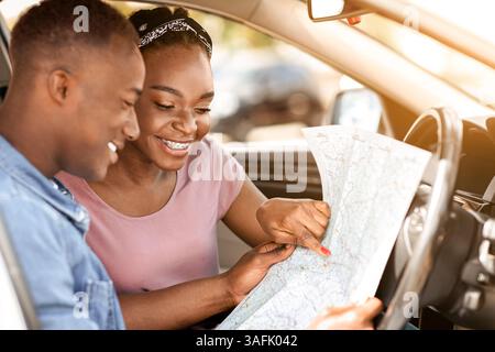 Enthusiastic black couple reading map while having car trip Stock Photo