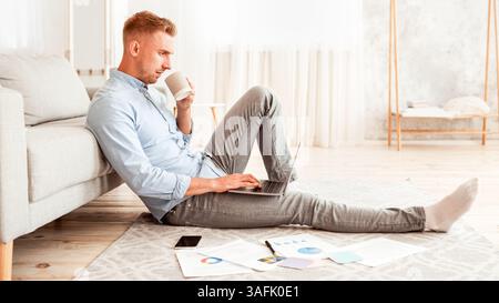 Focused man sitting on floor using phone drinking coffee Stock Photo