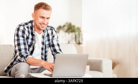 Happy man using laptop sitting on couch Stock Photo