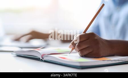 Unrecognizable african female secretary taking notes while working on laptop in office Stock Photo