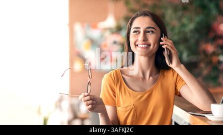 Happy female student talking on phone while studying at cafe Stock Photo
