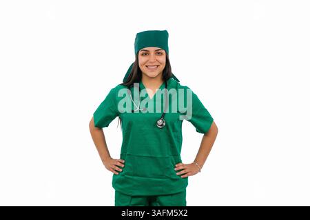 Young Latin woman doctor wearing a medical uniform and stethoscope, posing confidently with hands on hips and smiling brightly against a clean white b Stock Photo