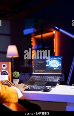Computer scientist using laptop, updating artificial intelligence neural networks, writing binary code scripts. Young remote employee working from home uses notebook, programming AI Stock Photo