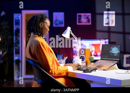 Computer scientist updating artificial intelligence neural networks, writing binary code scripts. Remote worker in apartment office uses digital device programming to upgrade AI Stock Photo