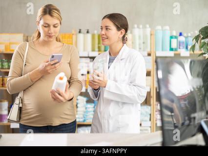 Pregnant woman using phone to check ingredients of cream with pharmacist guidance Stock Photo