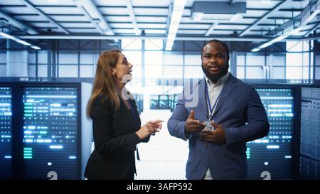 Teamworking colleagues looking at holograms in data center, working together. Server hub IT staff members doing brainstorming and interacting with augmented reality AI visualization, camera B Stock Photo