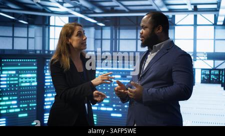 Teamworking colleagues looking at holograms in data center, working together. Server hub IT staff members doing brainstorming and interacting with augmented reality AI visualization, camera A Stock Photo