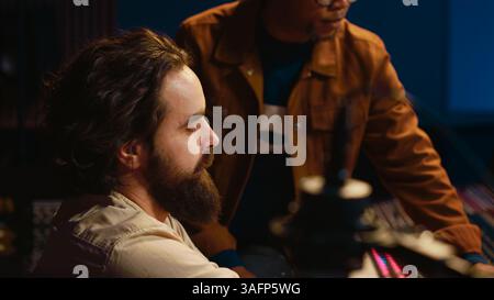 Musician and producer work on soundboard pads at professional studio station. Sound designer uses digital mixer in music production, operating on sliders and key buttons at control desk. Camera A. Stock Photo