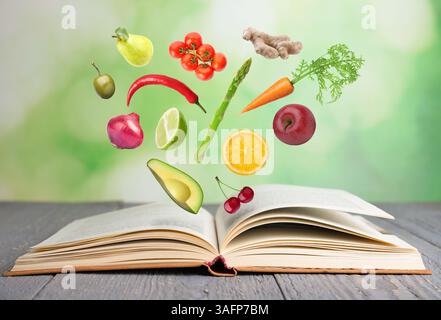 Fresh ingredients in air over recipe book on wooden table outdoors Stock Photo