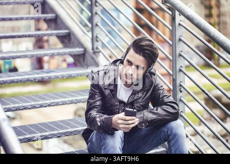 Handsome young man standing outdoors in urban environment on metal stairs, using cell phone Stock Photo